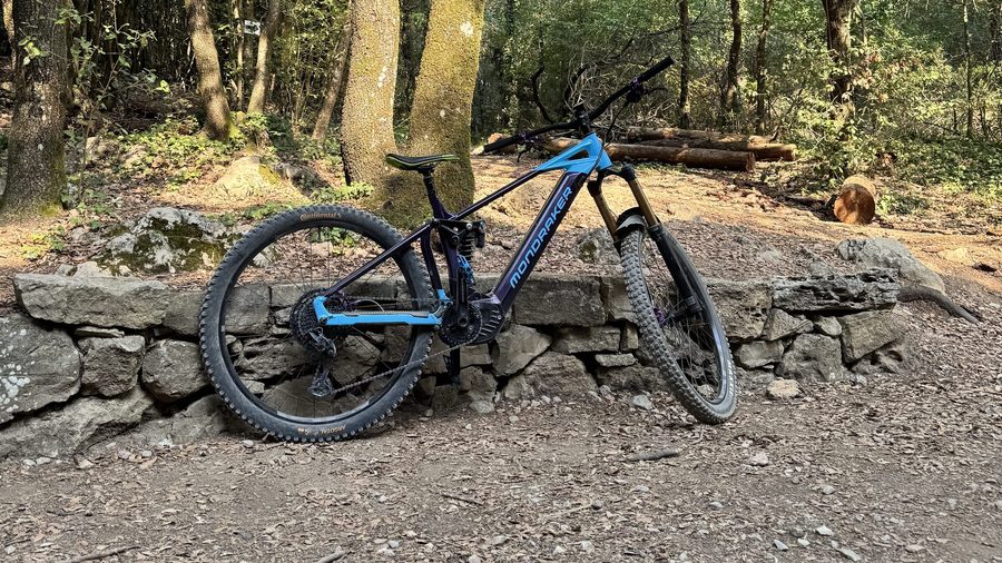 A Mondraker e-mountain bike leaning against a stone wall in the oak woods of Maremma.